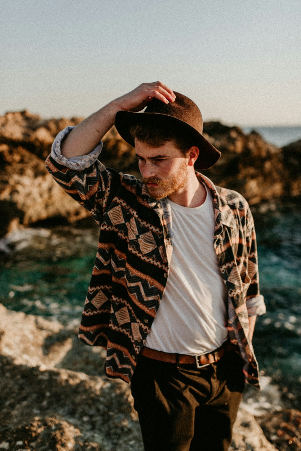 man in white tank top and black and brown tribal print cardigan wearing brown fedora hat