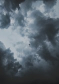 A lone airplane is silhouetted against a dramatic sky filled with dark, swirling clouds, suggesting an impending storm.
