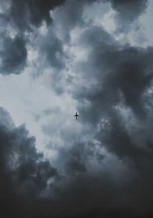A lone airplane is silhouetted against a dramatic sky filled with dark, swirling clouds, suggesting an impending storm.