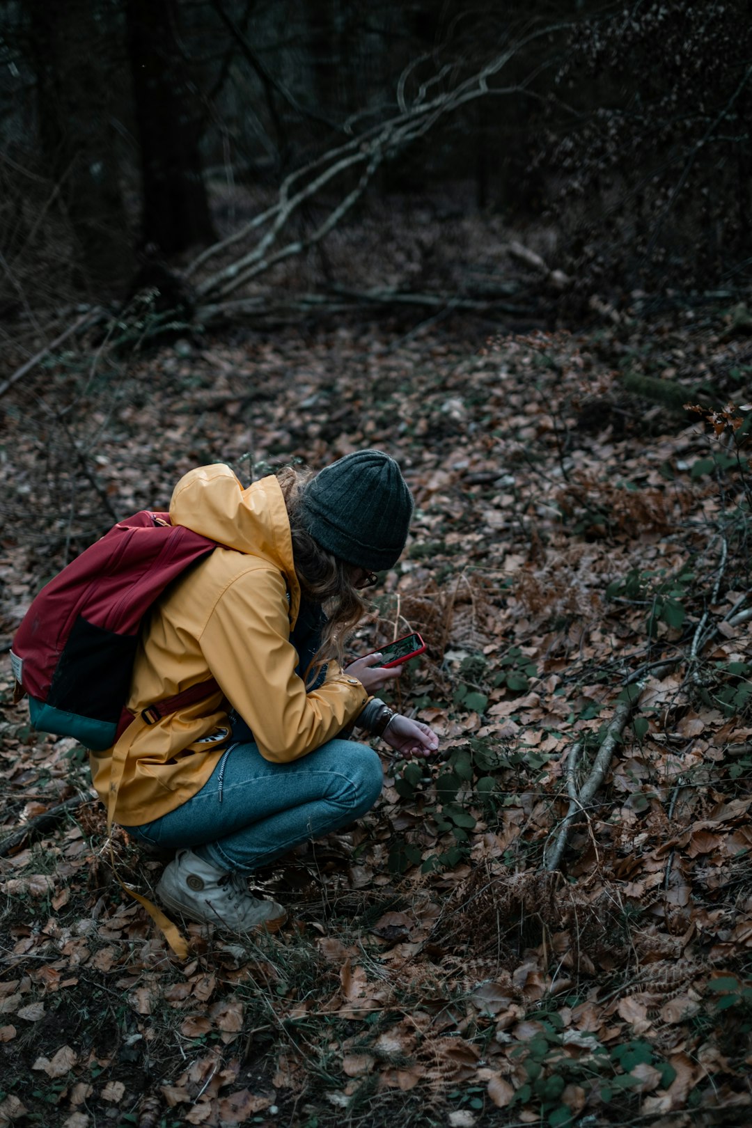 man in yellow jacket and blue denim jeans sitting on ground with dried leaves