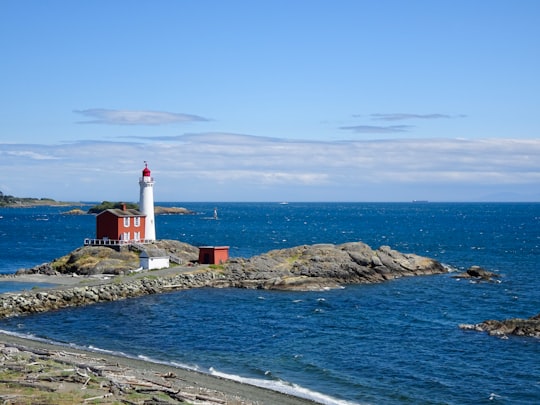 white and red lighthouse on rocky shore during daytime in Fisgard Lighthouse National Historic Site Canada