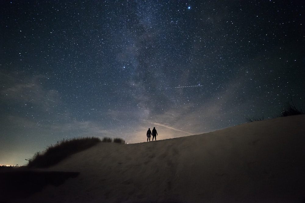 2 person walking on snow covered ground under starry night