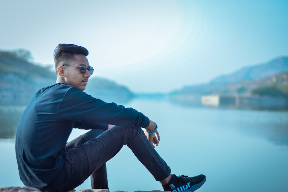 man in black long sleeve shirt and blue denim jeans sitting on rock during daytime