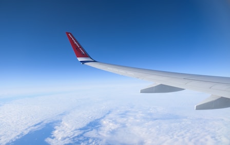 white and red airplane wing over white clouds during daytime