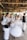 A group of people are engaged in traditional dance, wearing traditional or folkloric clothing. The setting is a rustic wooden building with large windows, and the movement of the dancers creates a dynamic and blurred effect.