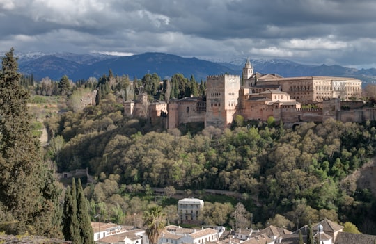 brown concrete building surrounded by green trees under blue sky during daytime in Alhambra Palace Spain