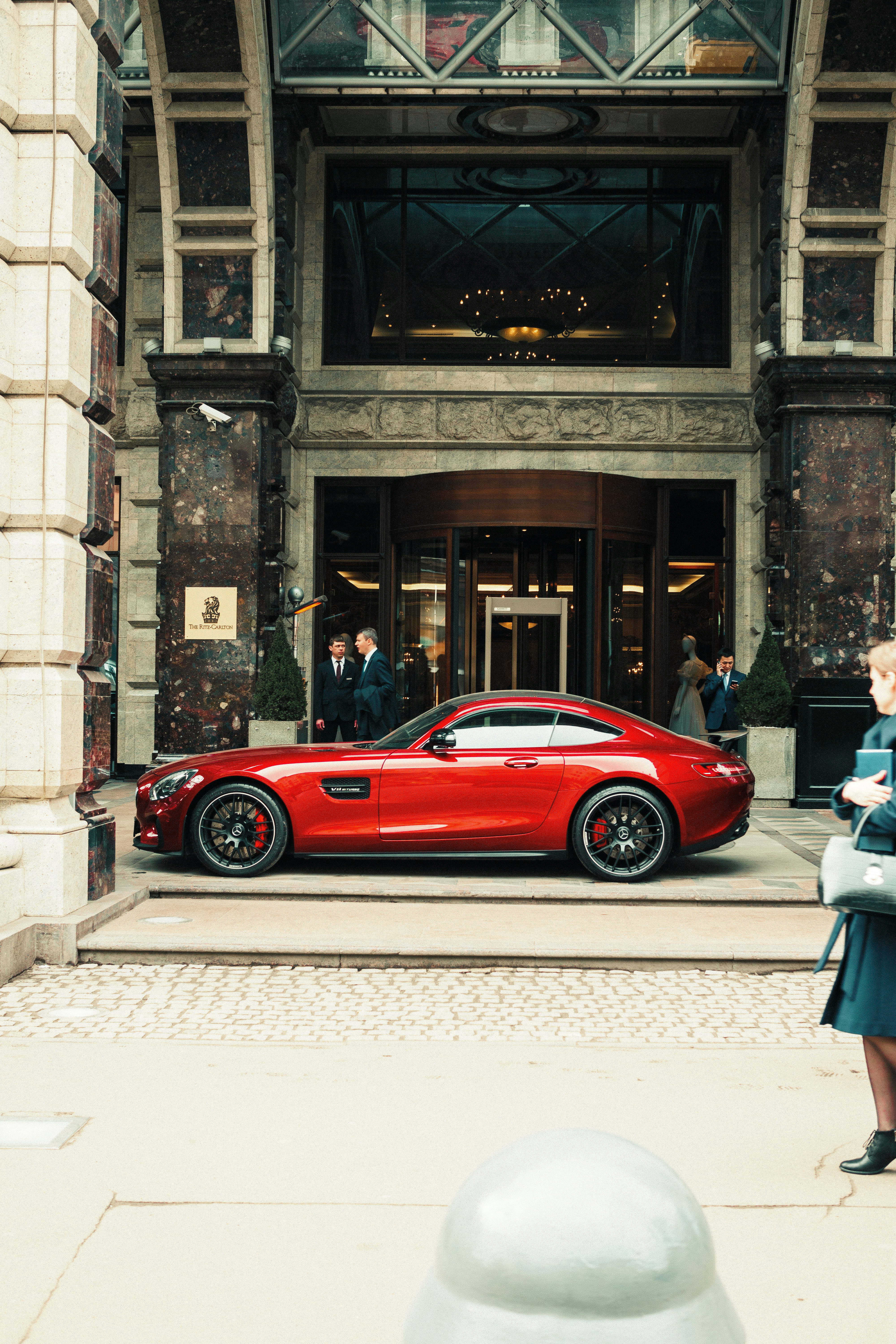 昼間、茶色のコンクリートの建物の脇に停車する赤いクーペ