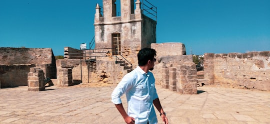 man in white t-shirt standing near brown concrete building during daytime in Diu Fort India