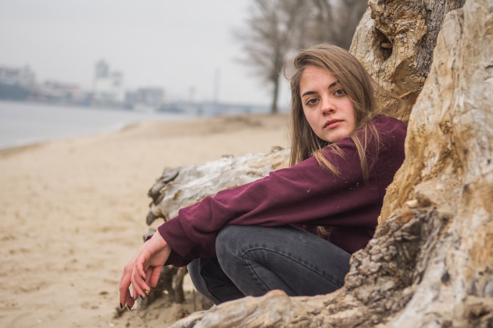 woman in purple hoodie and blue denim jeans sitting on brown rock during daytime