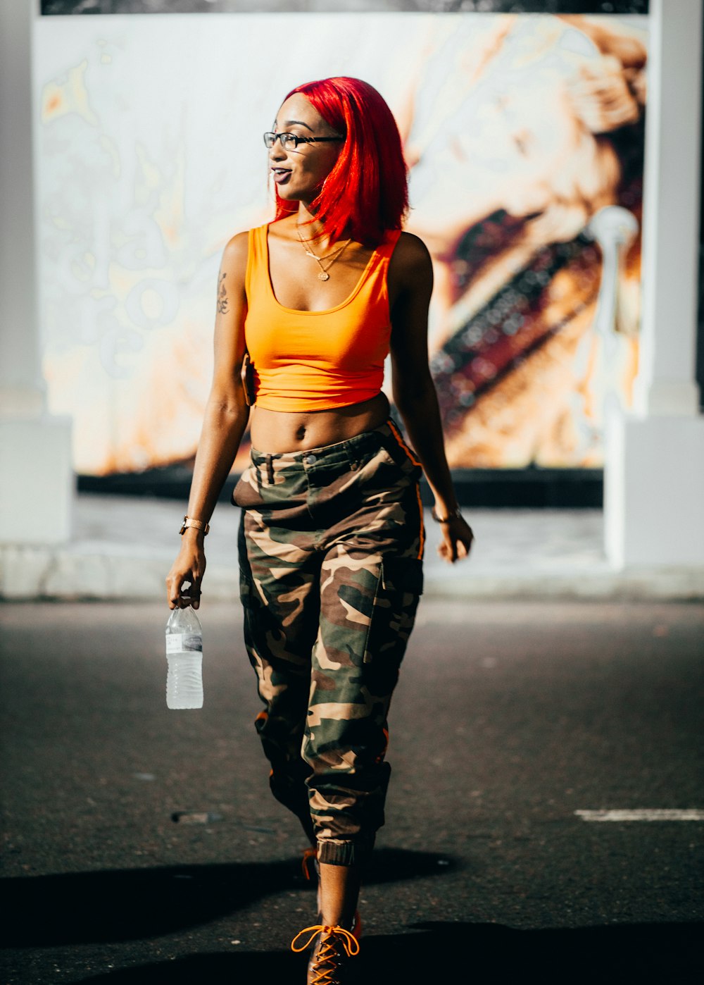 woman in orange tank top and camouflage pants standing on road during daytime