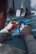 A person uses pliers to work on a small electronic component on a table. There is a soldering station and other tools in the background. The environment appears to be a workshop or electronics lab.