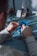 A person uses pliers to work on a small electronic component on a table. There is a soldering station and other tools in the background. The environment appears to be a workshop or electronics lab.
