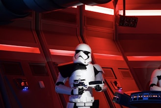 A futuristic and dimly lit room featuring a person in white armored attire holding a blaster. The background consists of panels and red neon lights, creating a sci-fi ambiance.