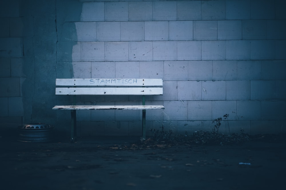 white wooden bench beside blue brick wall