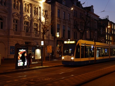 people walking on sidewalk near white and yellow tram during daytime