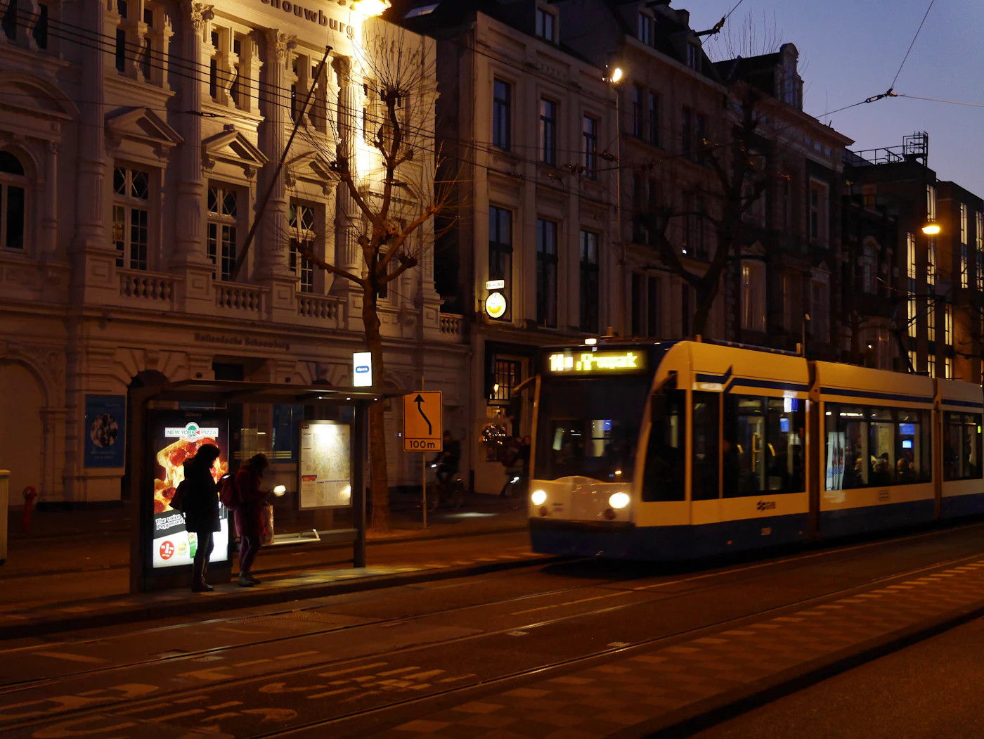 A yellow tram moving along a city street past pedestrians