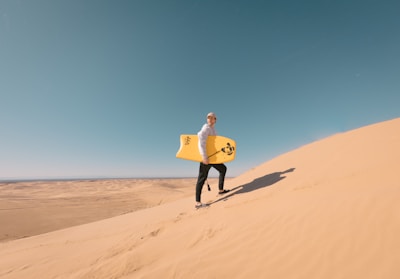 A person sandboarding down golden dunes under a bright blue sky in the Sahara.