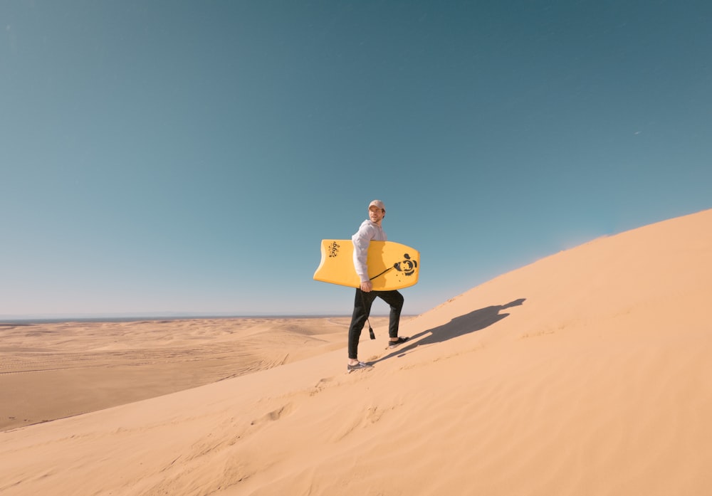 man in yellow jacket holding blue surfboard walking on brown sand during daytime