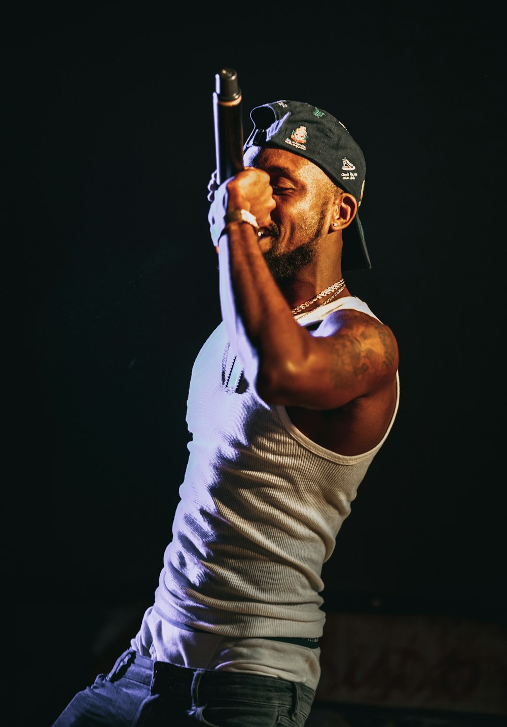 man in white tank top and gray cap holding microphone