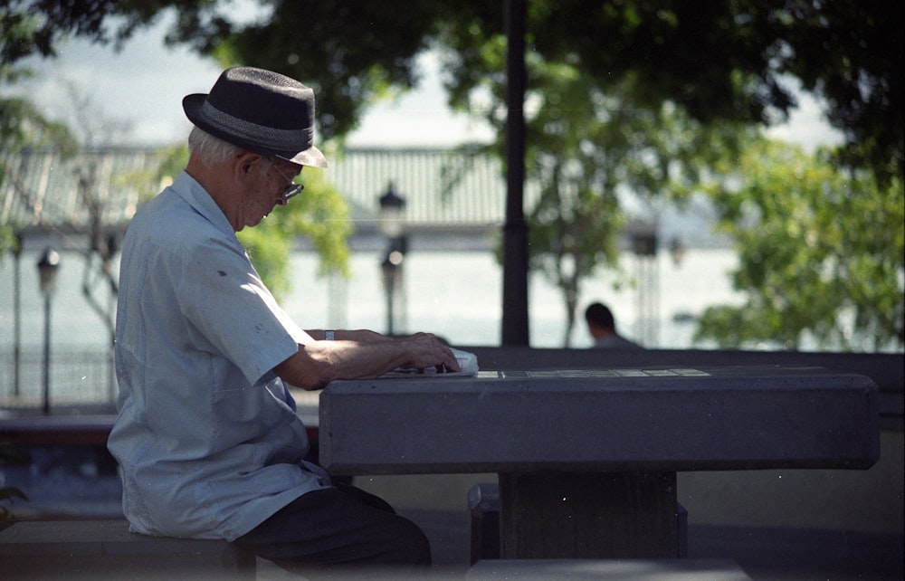 Mann im weißen Hemd und schwarzem Fedora-Hut sitzt auf der Bank