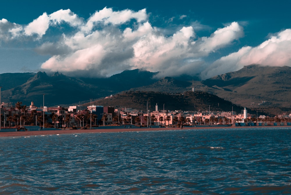 body of water near mountain under white clouds and blue sky during daytime