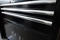 A black metal cabinet with several horizontal shiny metal handles. The cabinet appears to have multiple drawers and lower storage doors. The smooth surface reflects some light, giving it a polished appearance.