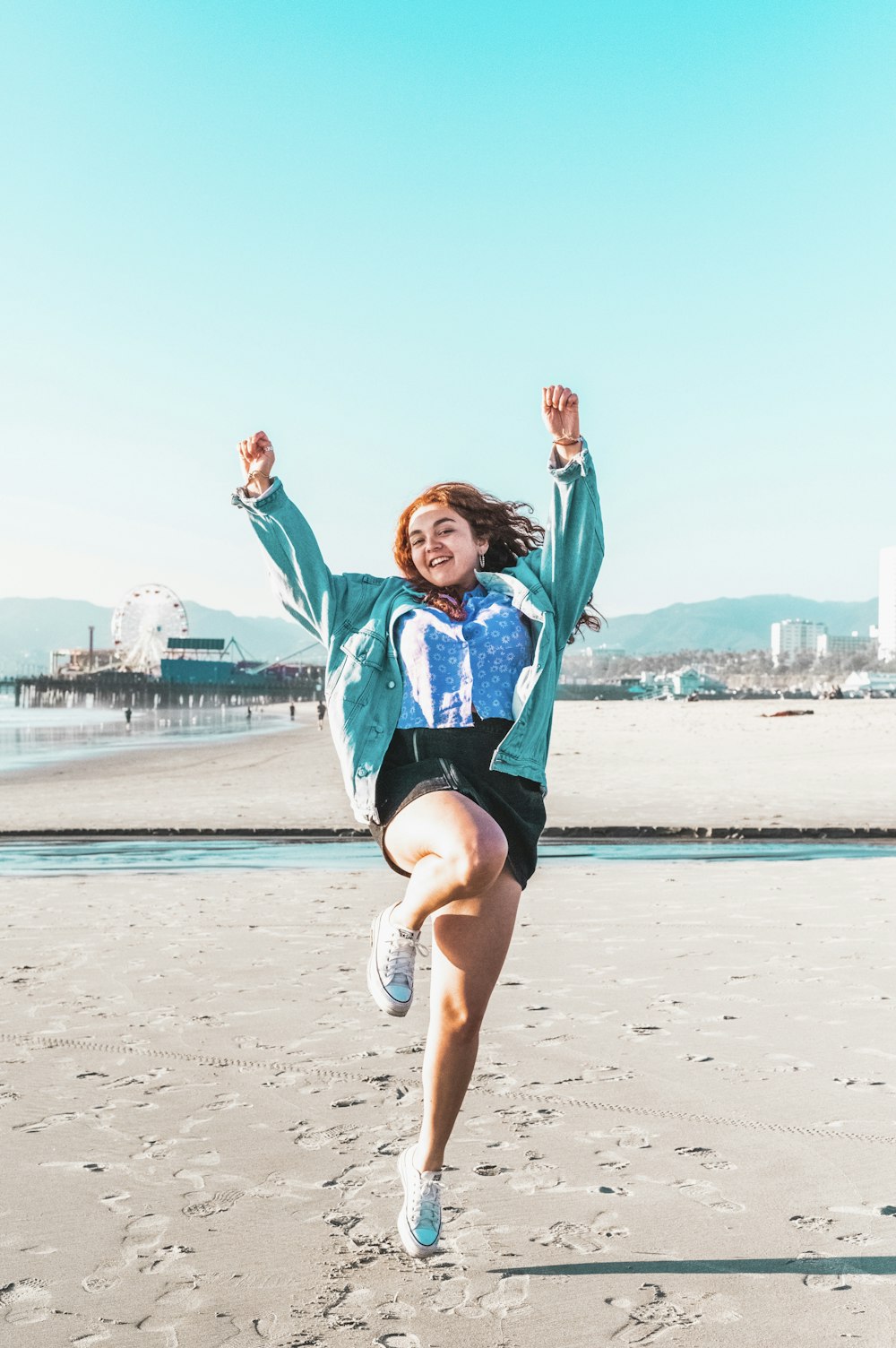 woman in blue jacket and black shorts jumping on beach during daytime