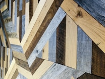 An intricate pattern of wooden planks arranged in a geometric design, featuring a variety of wood textures and shades. The planks are meticulously fitted together to form a visually appealing structure with alternating colors.