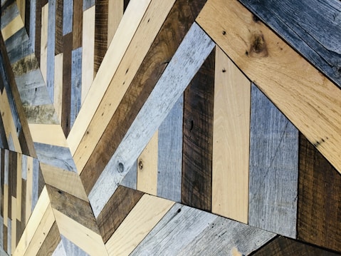An intricate pattern of wooden planks arranged in a geometric design, featuring a variety of wood textures and shades. The planks are meticulously fitted together to form a visually appealing structure with alternating colors.