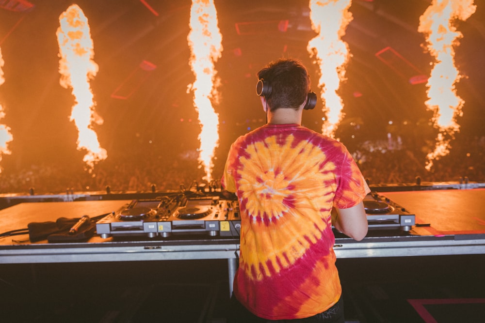 man in red and yellow tie dye shirt standing in front of dj controller