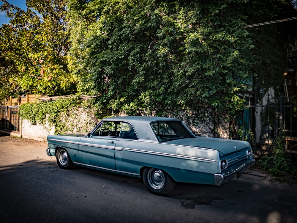 Blauer Oldtimer tagsüber neben grünem Baum geparkt