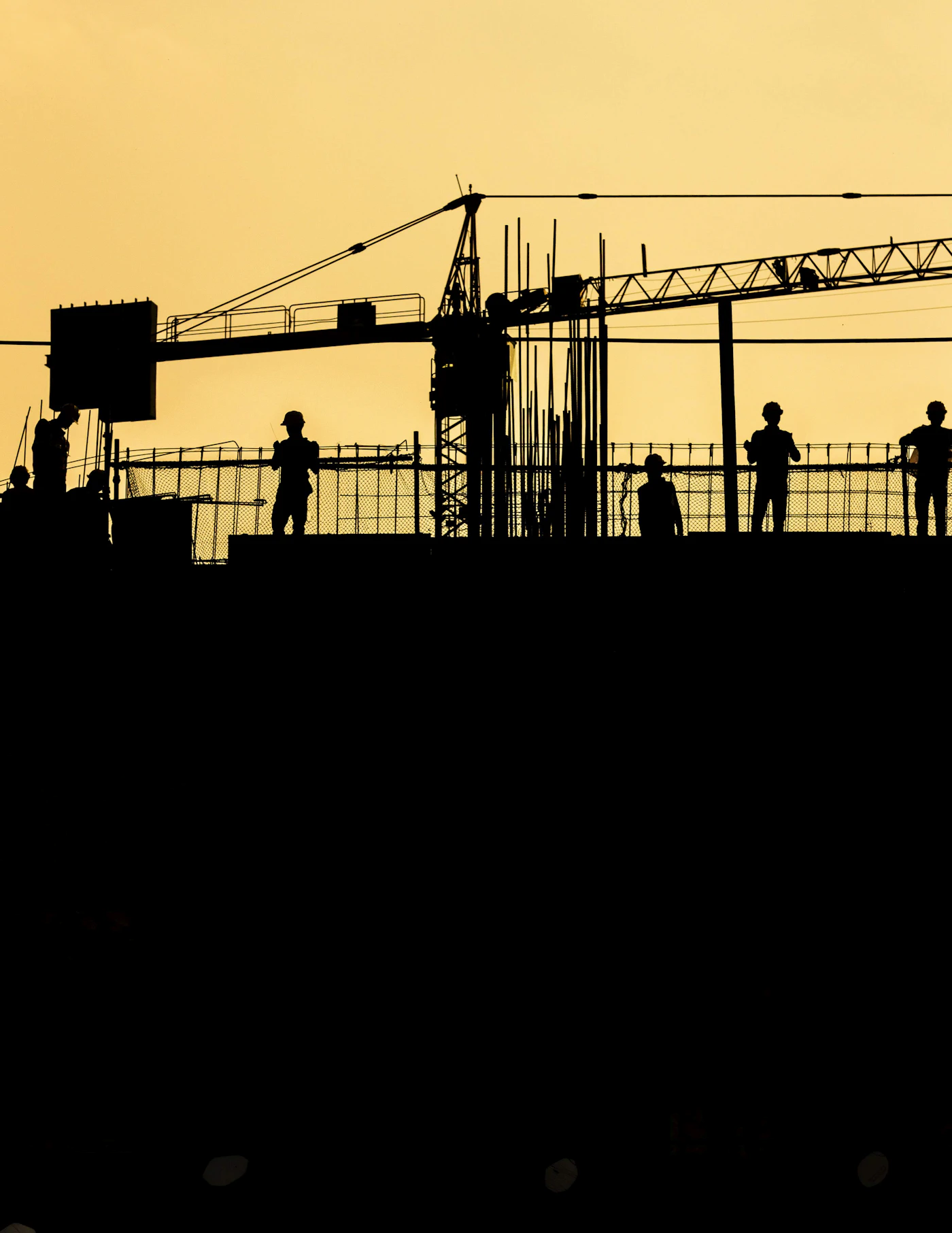 Construction crew silhouetted against a golden sunset sky at a high-rise site