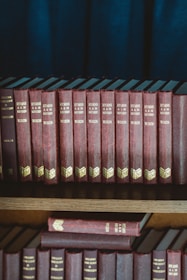 red and black hardbound books on brown wooden shelf