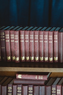 red and black hardbound books on brown wooden shelf