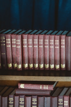 red and black hardbound books on brown wooden shelf