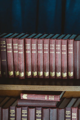 red and black hardbound books on brown wooden shelf
