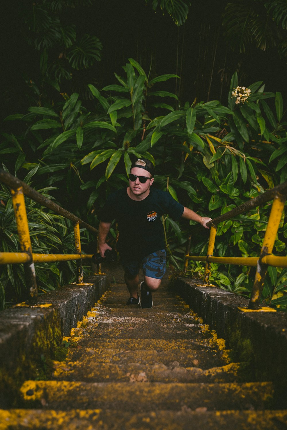 man in black crew neck t-shirt and blue denim jeans walking on wooden bridge