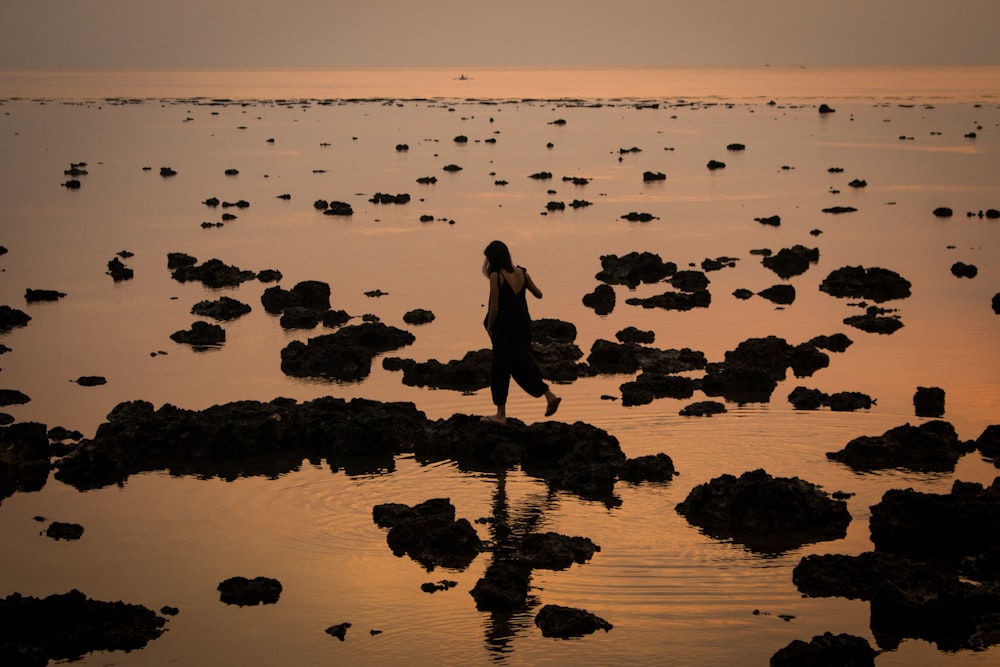 silhouette of woman standing on rock formation near body of water during daytime