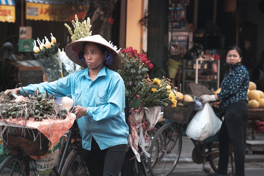 woman in blue dress shirt and black skirt holding red bicycle with white flowers