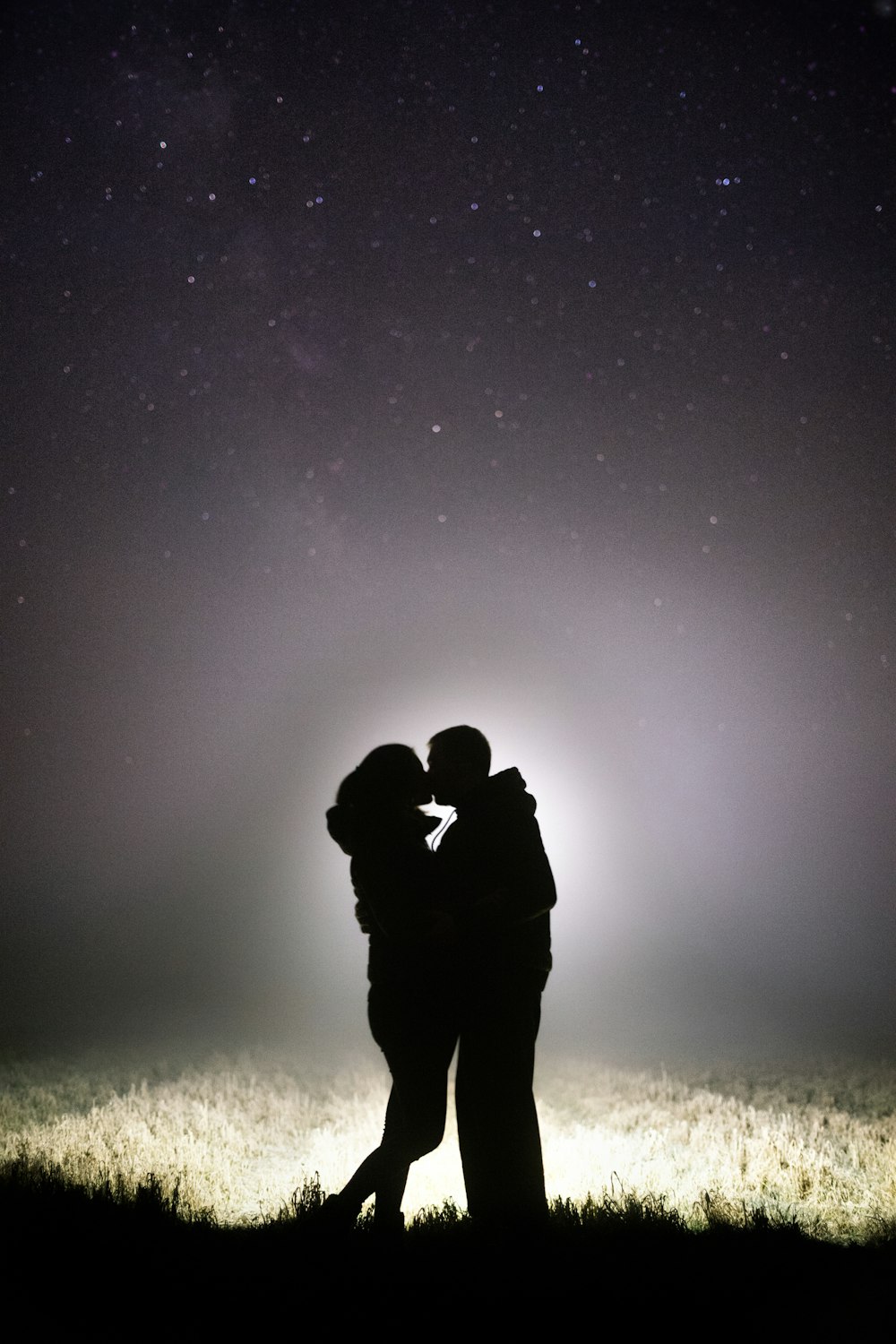 silhouette of man and woman kissing under starry night