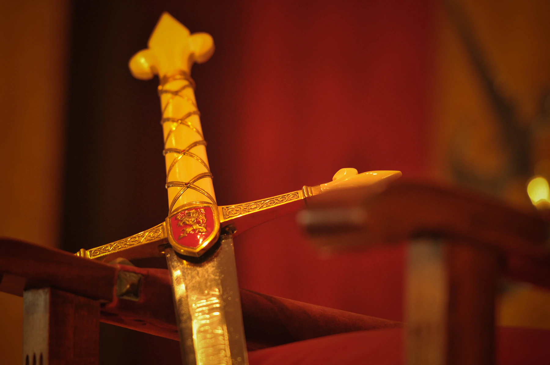 A sword with a gilt hilt and a red enamel crest resting on a red stand