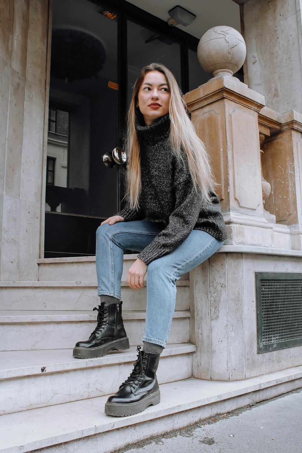 woman in black sweater and blue denim jeans sitting on gray concrete bench