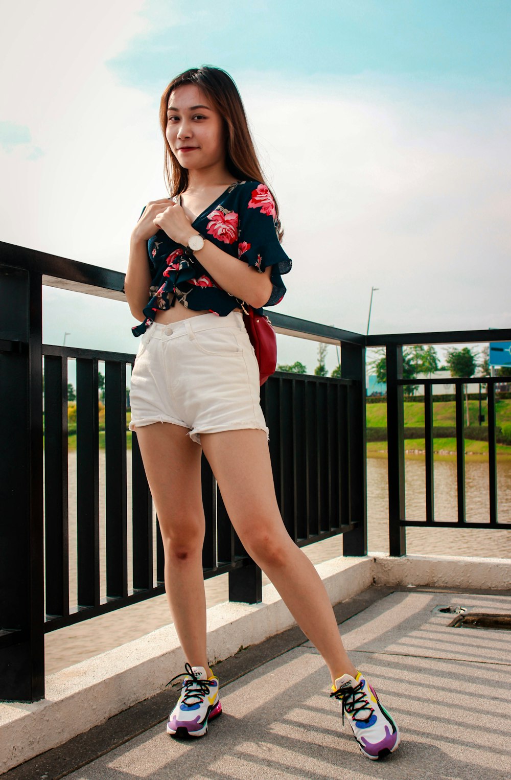 woman in black and red floral shirt and white shorts standing beside black metal fence during