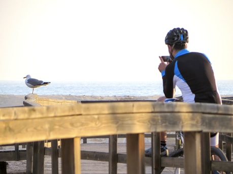 man in blue long sleeve shirt and black pants sitting on brown wooden dock during daytime