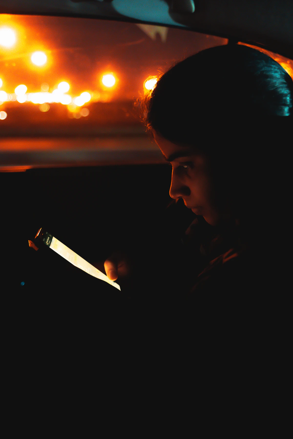 A face lit by a phone screen inside a car at night