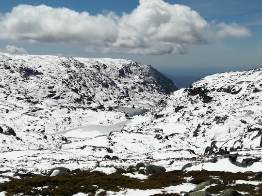 snow covered mountain under white clouds and blue sky during daytime in Serra da Estrela Portugal