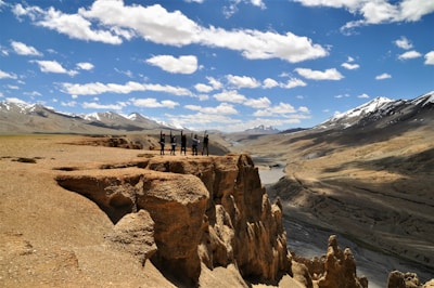 people walking on brown dirt road near gray mountains under blue and white sunny cloudy sky