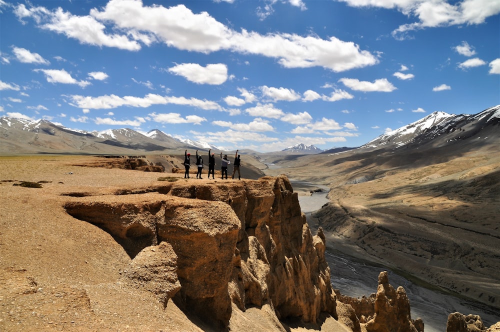 people walking on brown dirt road near gray mountains under blue and white sunny cloudy sky