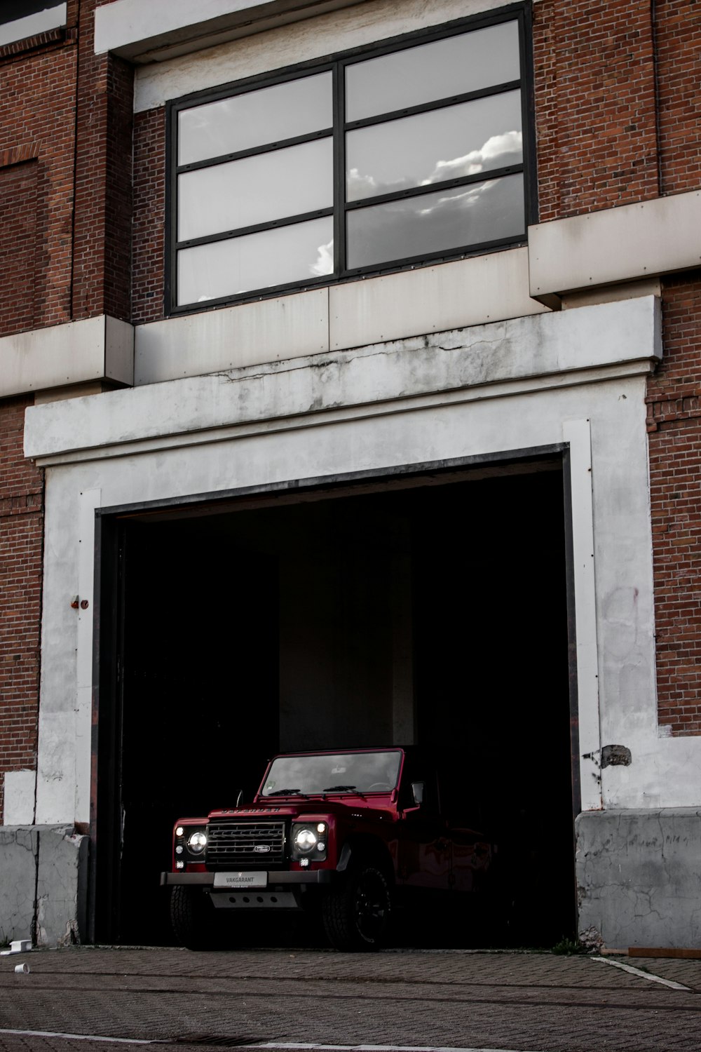 白いコンクリートの建物の前に停まる赤い車
