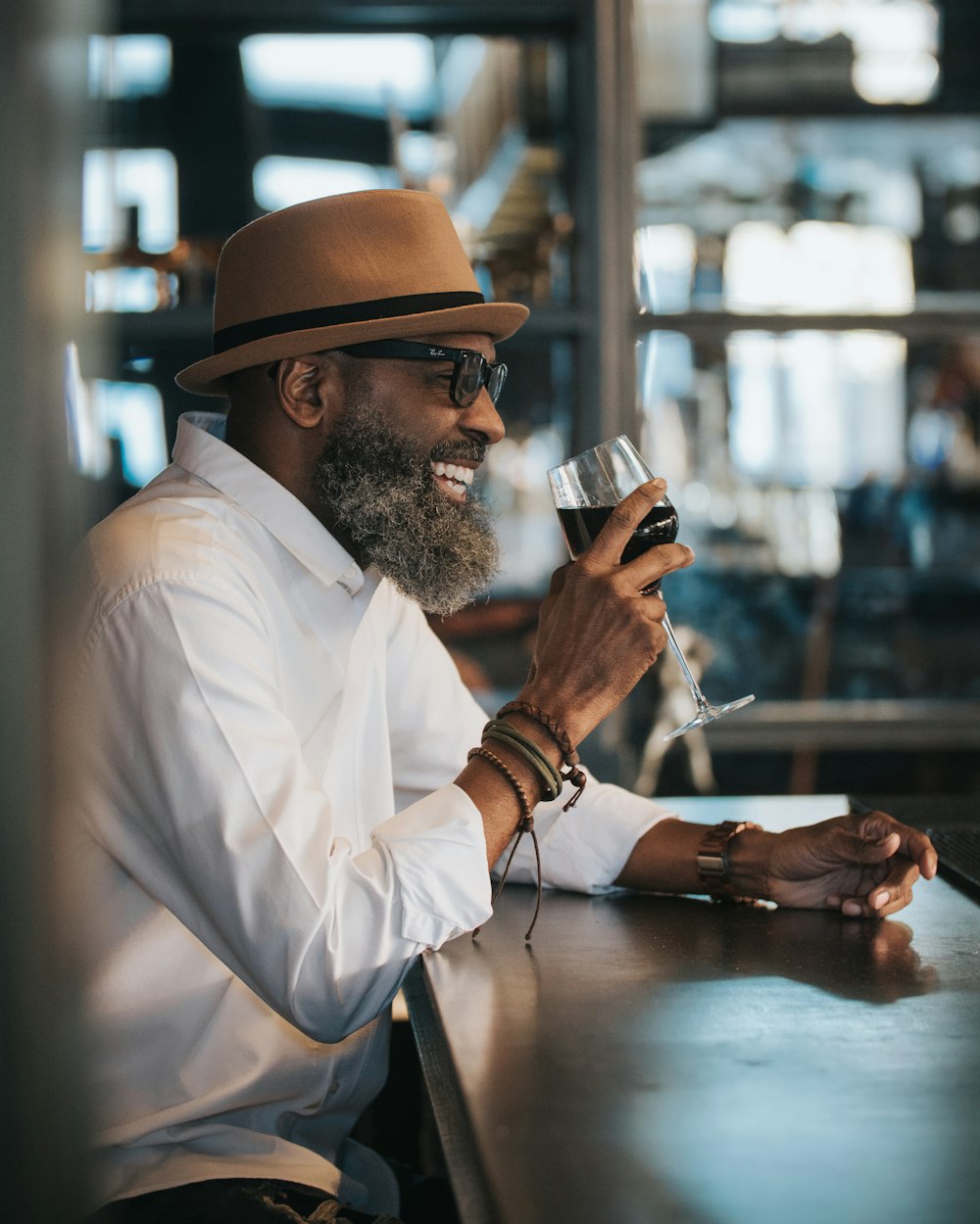 man in white dress shirt and brown hat holding clear drinking glass